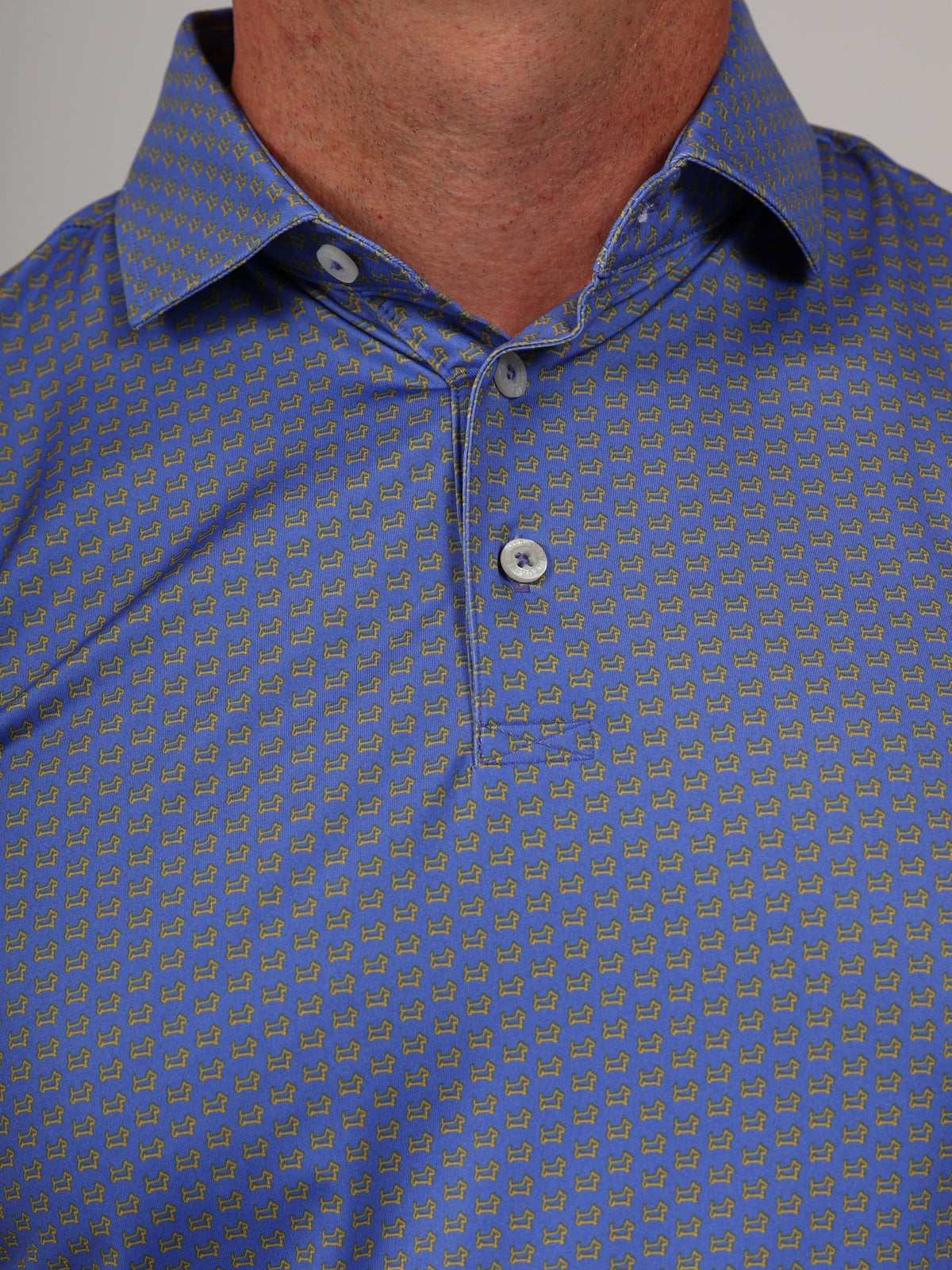 Close-up of a blue shirt with a small, repeating pattern of yellow scottish dogs. The shirt has a button-down collar and two visible buttons, conveying a casual yet stylish tone.