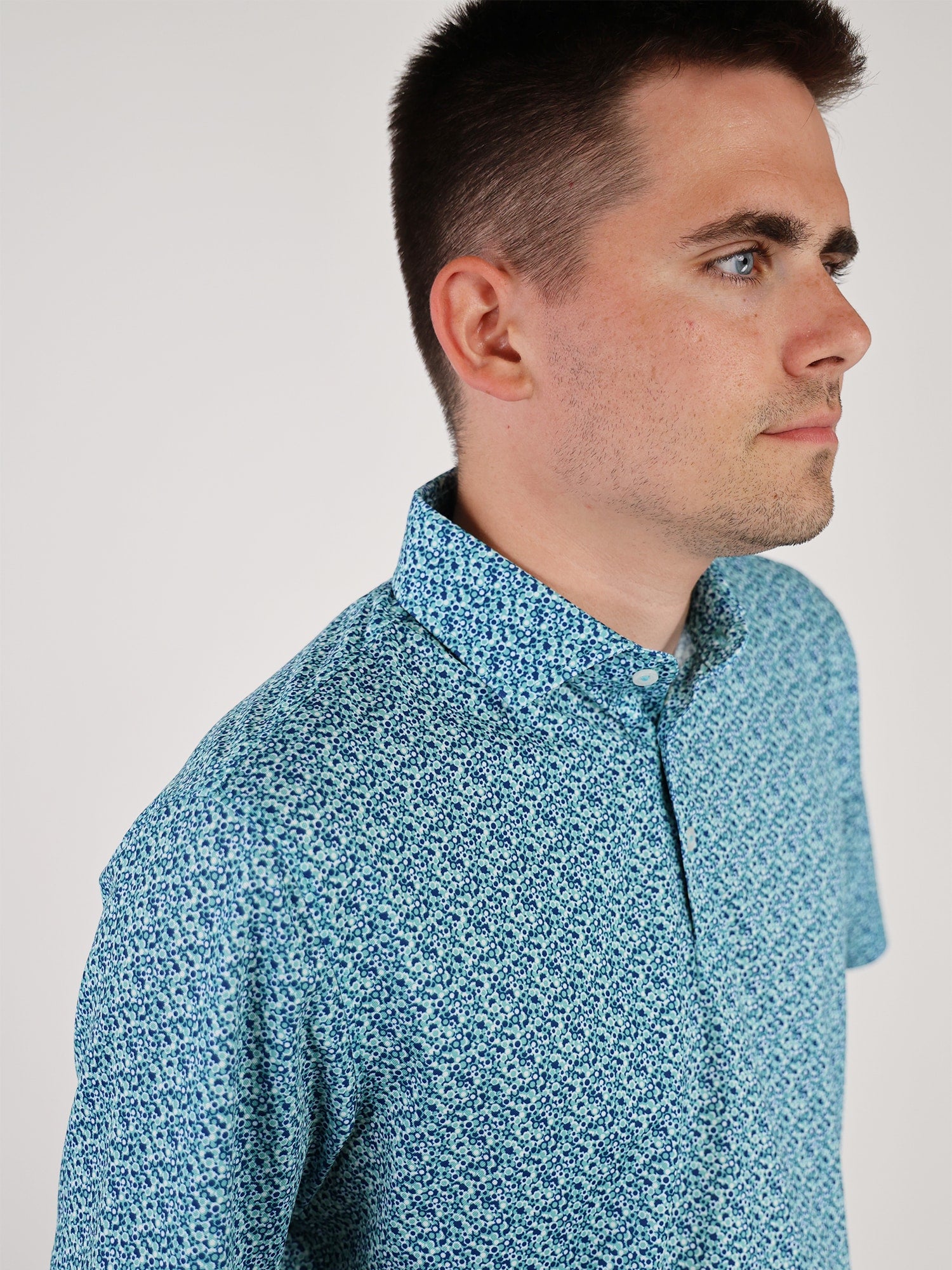 A person wearing a blue patterned button-up shirt looks to the right. The background is plain white