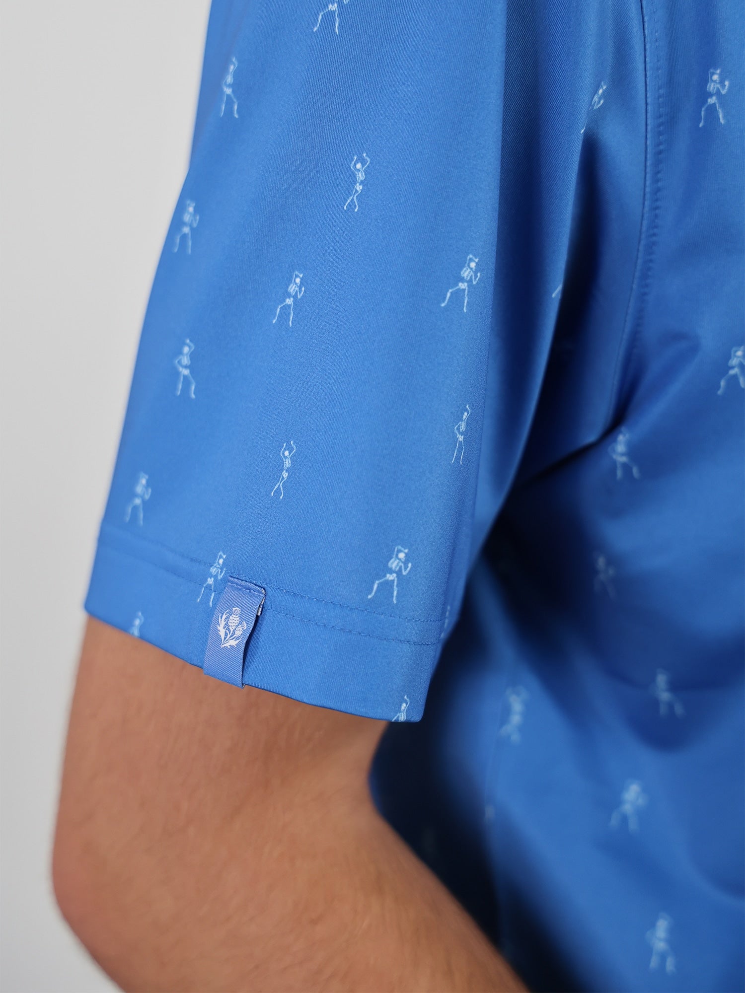 A close-up of a blue shirt sleeve with small white golfer motifs
