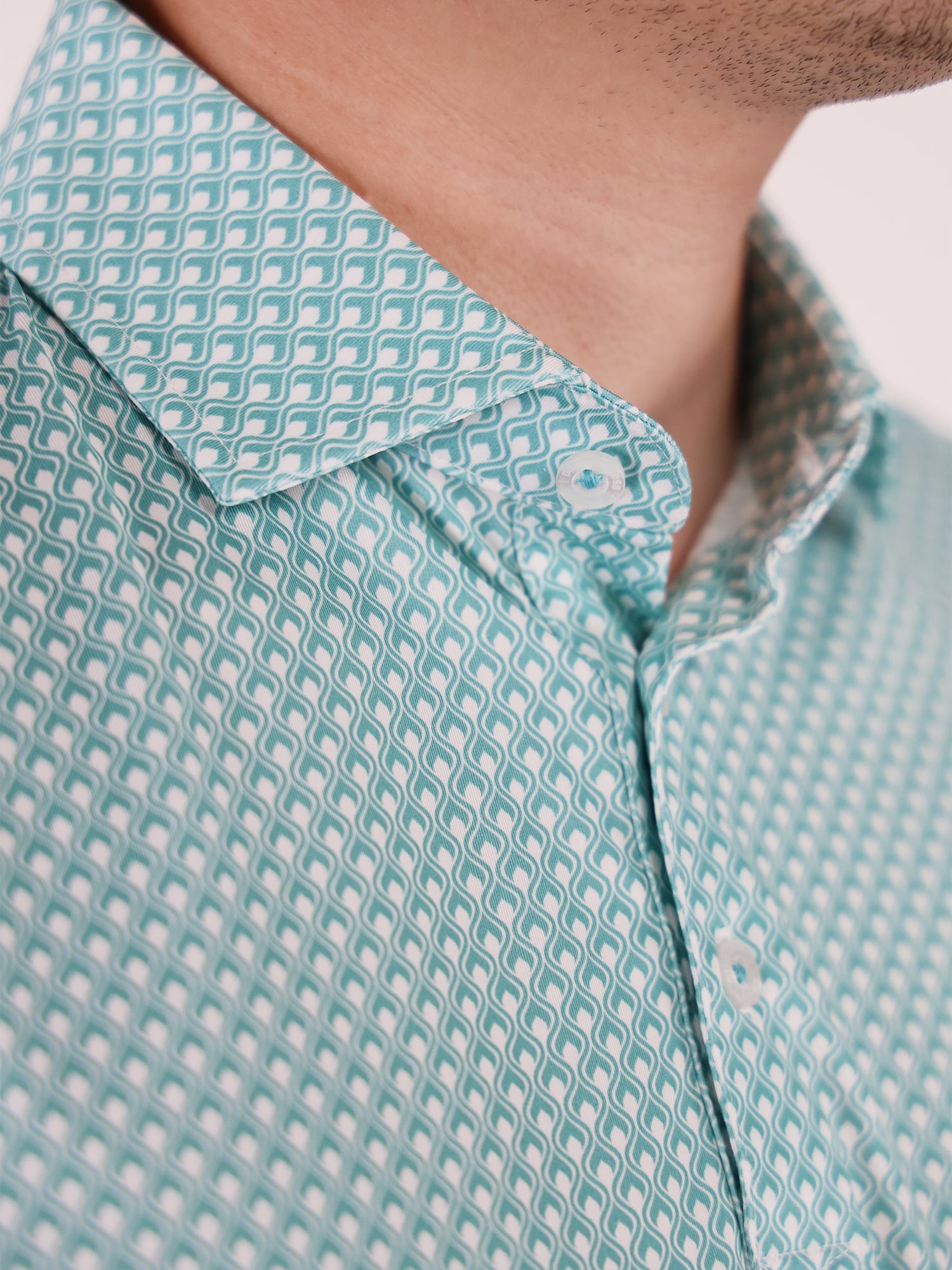 Close-up of a man wearing a teal patterned polo shirt with a soft flame printed design. The collar is neatly folded, and the three-button placket is partially unbuttoned