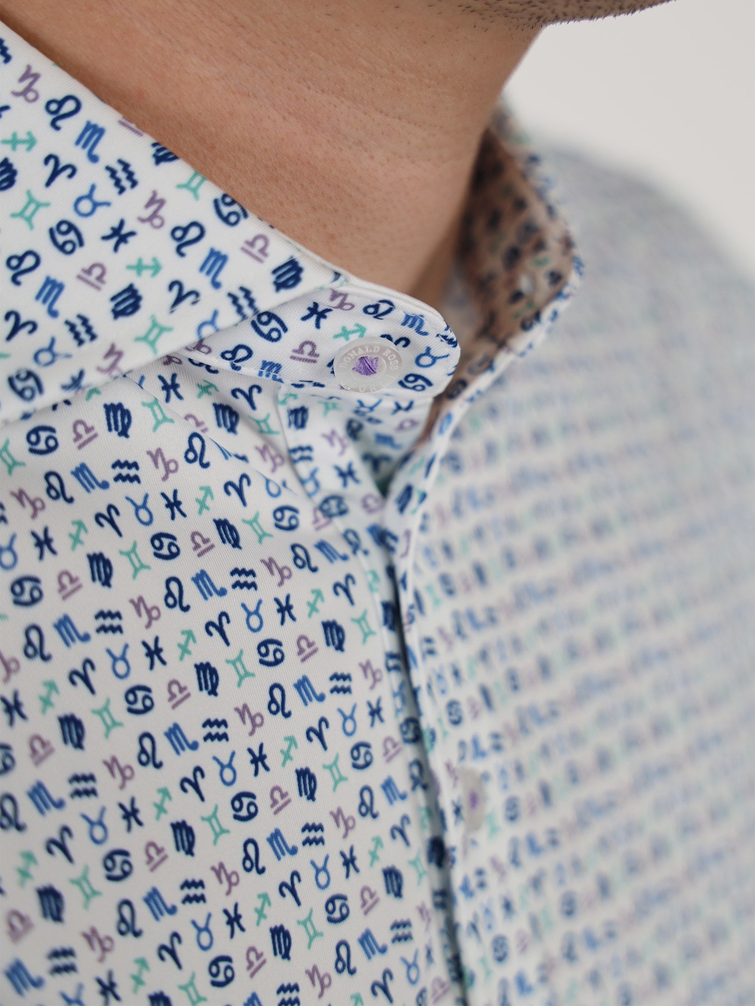 Close-up of a man wearing a white poloshirt featuring colorful, small zodiac symbols pattern in blue, green, and purple