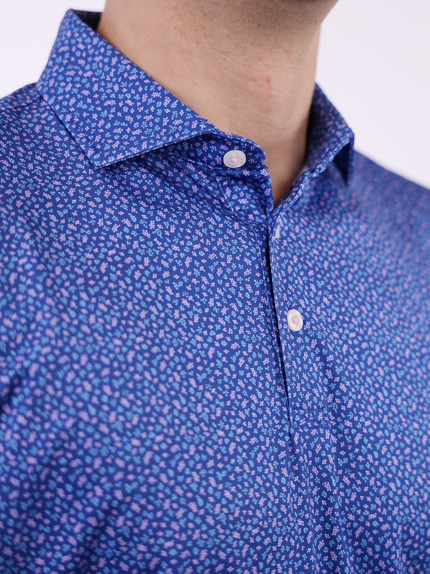 Close-up of a man wearing a dark blue collared shirt with a pattern of small blue and purple berries