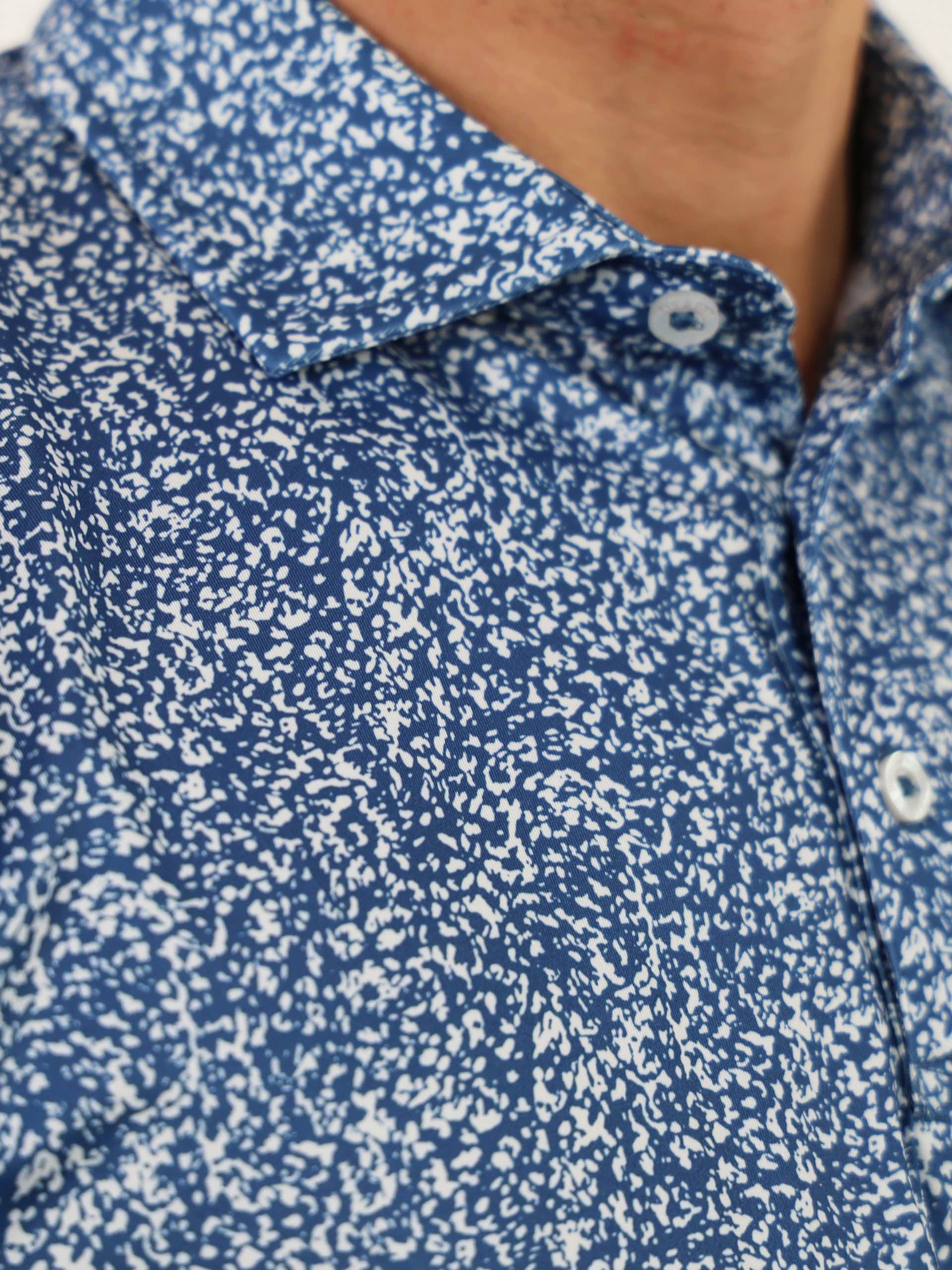 Close-up of a person wearing a blue shirt with a white sponge pattern. The shirt has a pointed collar and white buttons.