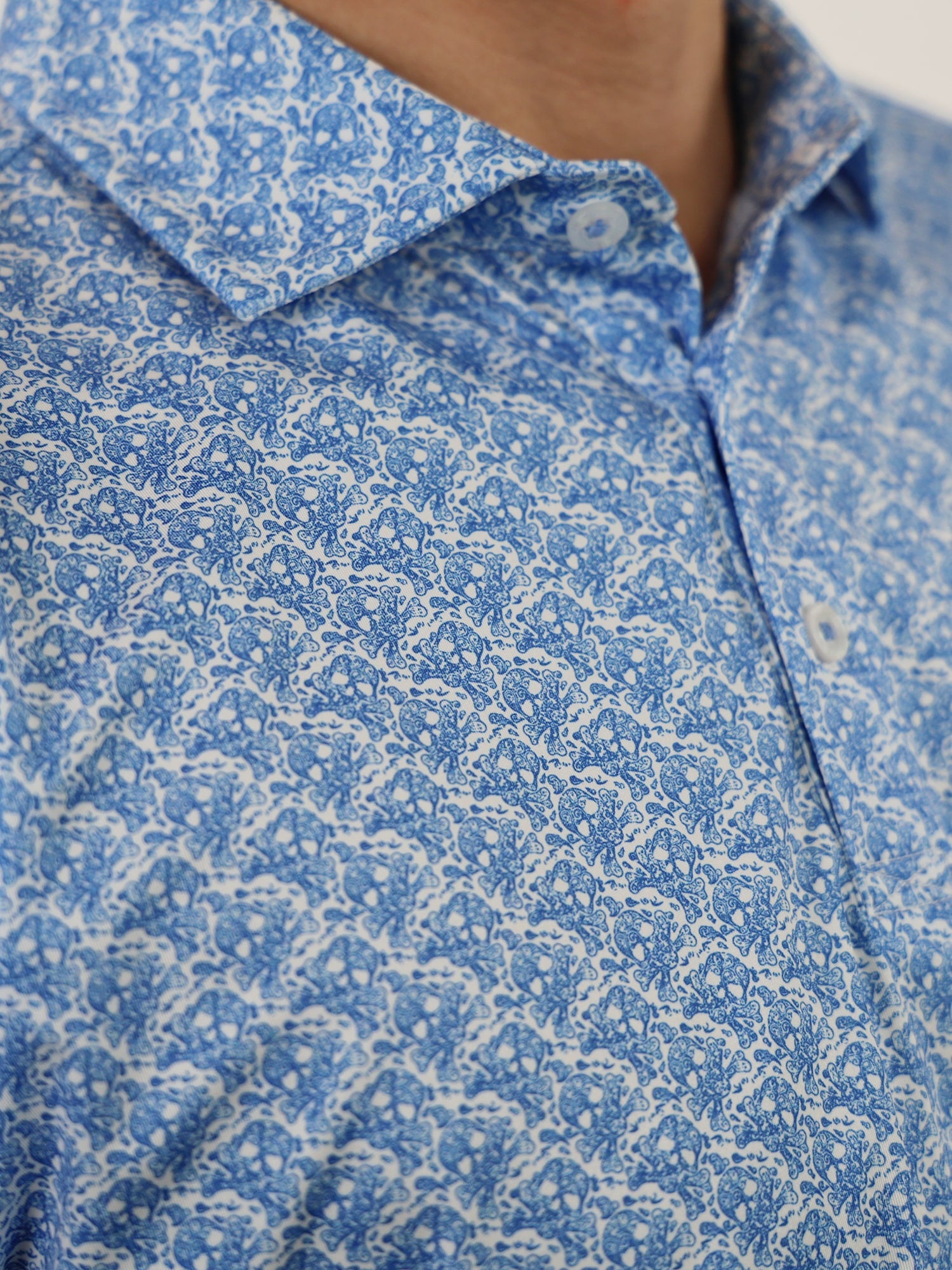 Close-up of a man wearing a blue paisley polo shirt with a subtle skull pattern and white buttons