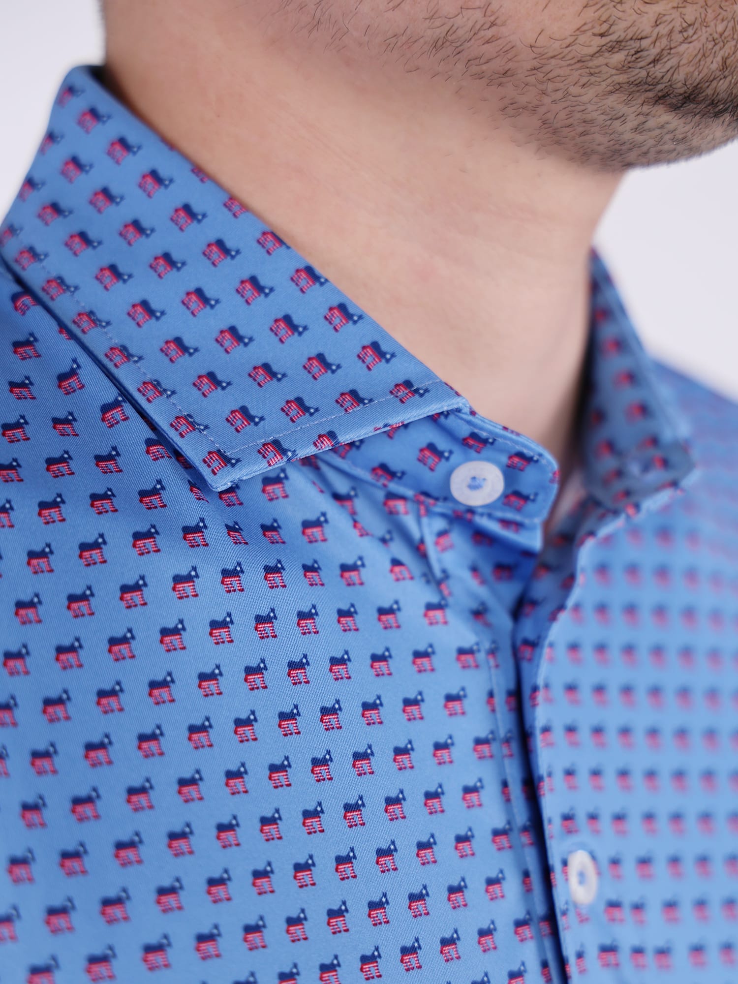 Close-up of a blue golf polo shirt featuring a repeating pattern of democrat donkeys in red and blue