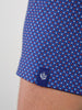 Close-up of blue fabric with red and white polka dots, featuring a small blue tag with a white thistle emblem at the hem