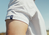 Person wearing a white mesh polo shirt with a small navy emblem on the sleeve against a clear blue sky.