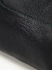 Close-up of black textured leather with a subtle embossed logo, featuring fine green stitching