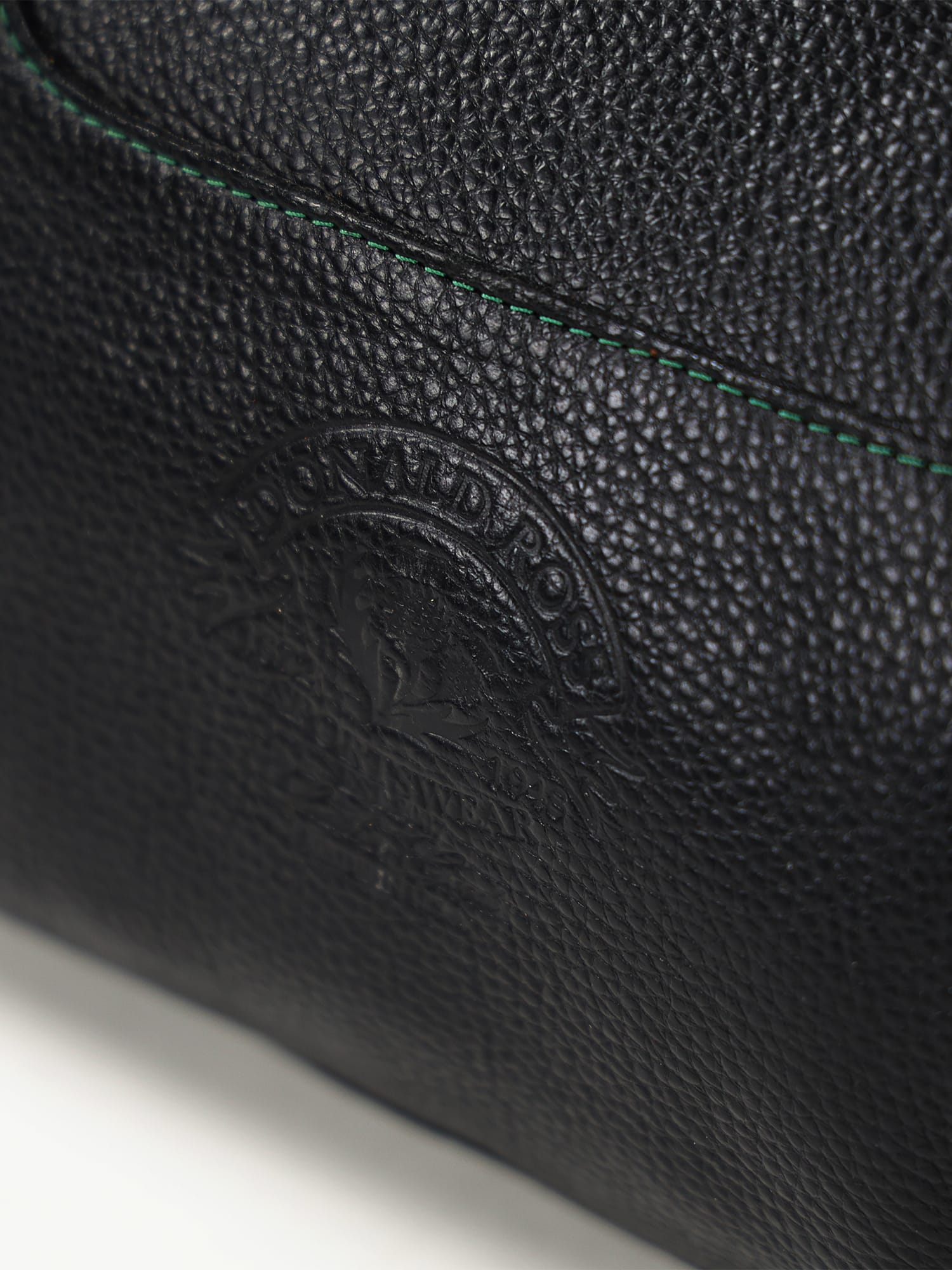 Close-up of black textured leather with a subtle embossed logo, featuring fine green stitching