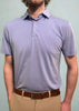 A man is standing straight and looking ahead while wearing a light purple polo shirt and beige pants.