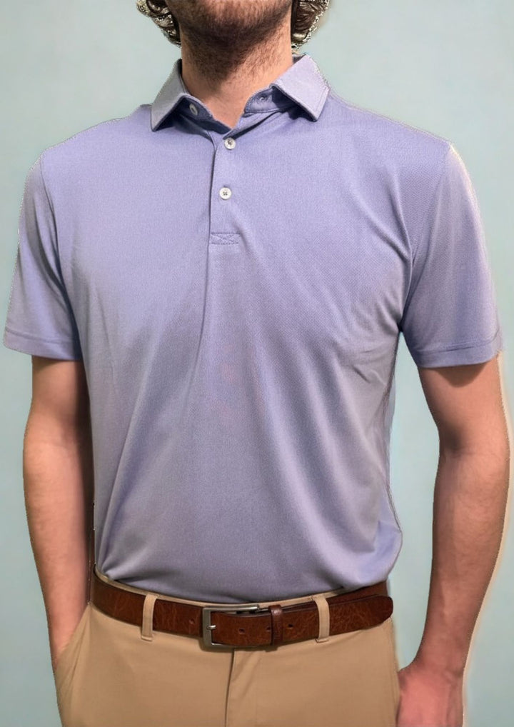 A man is standing straight and looking ahead while wearing a light purple polo shirt and beige pants.