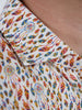 Close-up of a shirt collar with a vibrant, intricate dreamcatcher and feather pattern in blue, red, and yellow on a white background