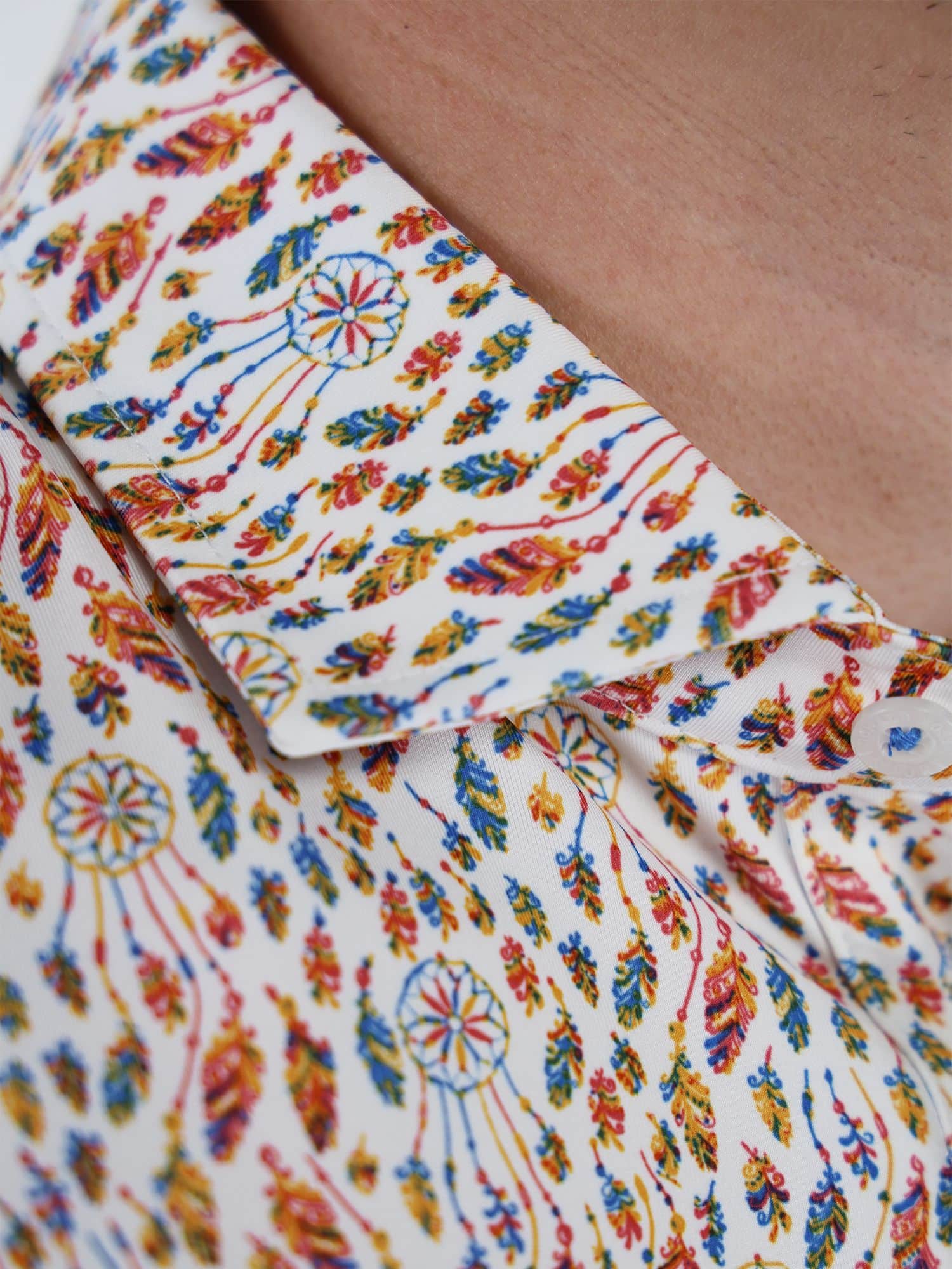 Close-up of a shirt collar with a vibrant, intricate dreamcatcher and feather pattern in blue, red, and yellow on a white background