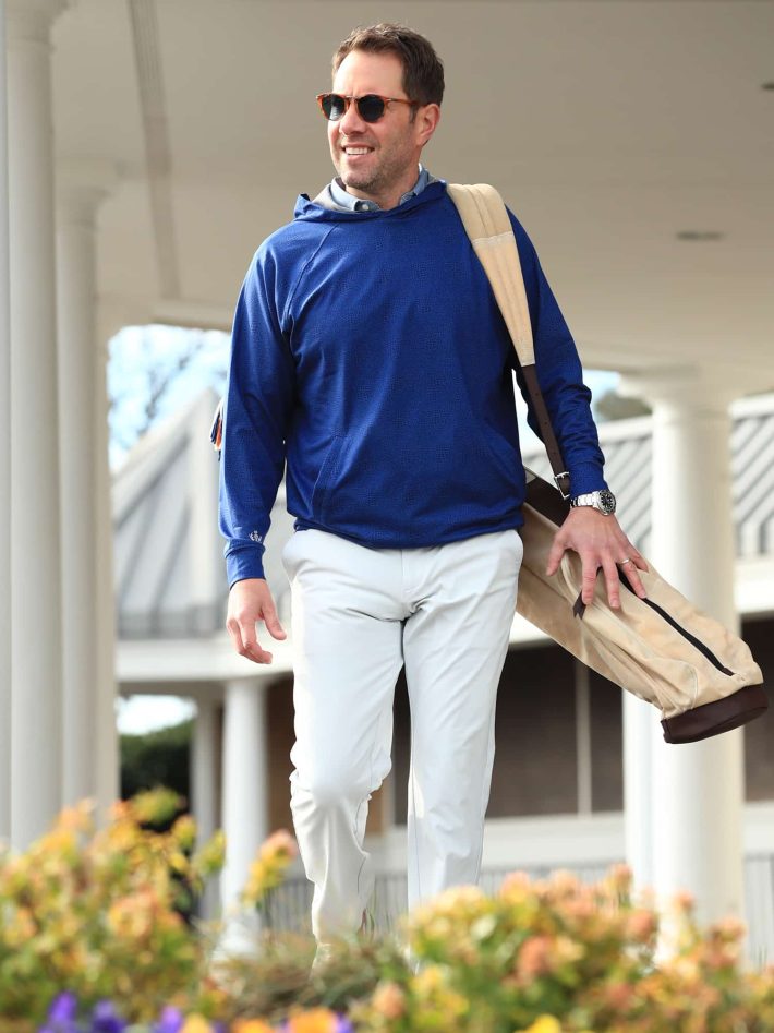 A man walking with a golf bag wears an alligator print golf hoodie.