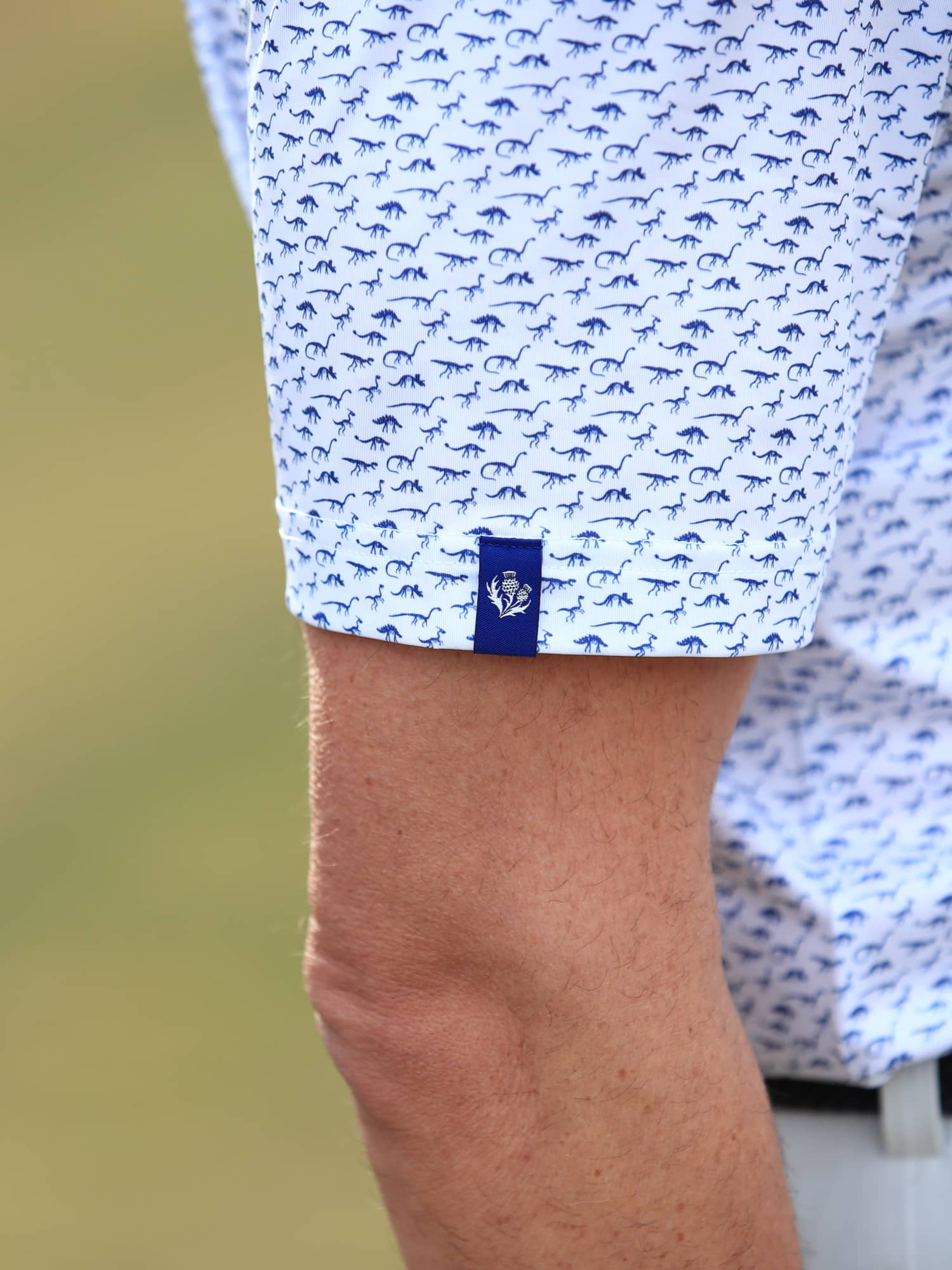 Close-up on the sleeve of a men's dinosaur fossils print polo in white and navy.
